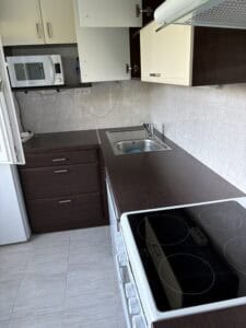 Sötét és világos konyhai szekrények, elektromos főzőlap és mikró, tiszta környezet.